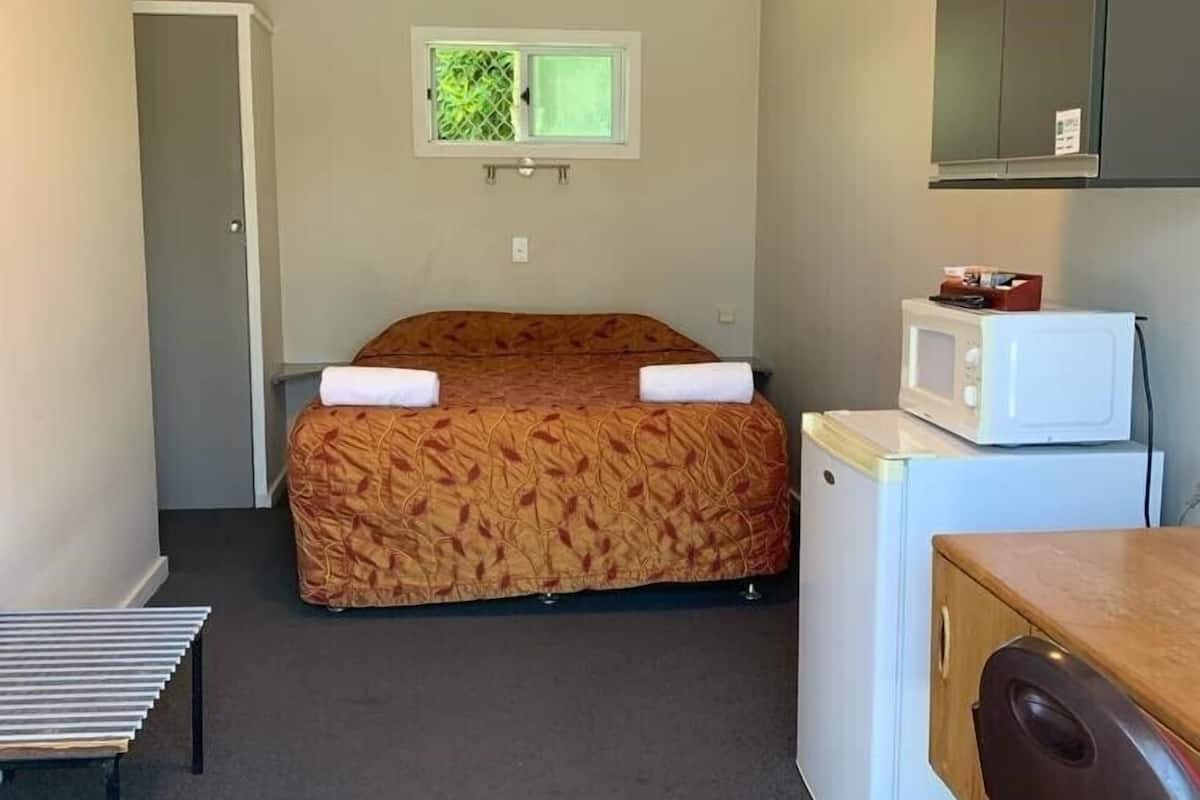 A compact room with a bed, a small kitchenette, a microwave, and a single chair.