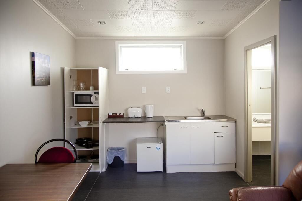 Cocina compacta con microondas, tostadora y lavamanos. Incluye un refrigerador pequeño, un basurero y una ventana sobre el lavamanos.