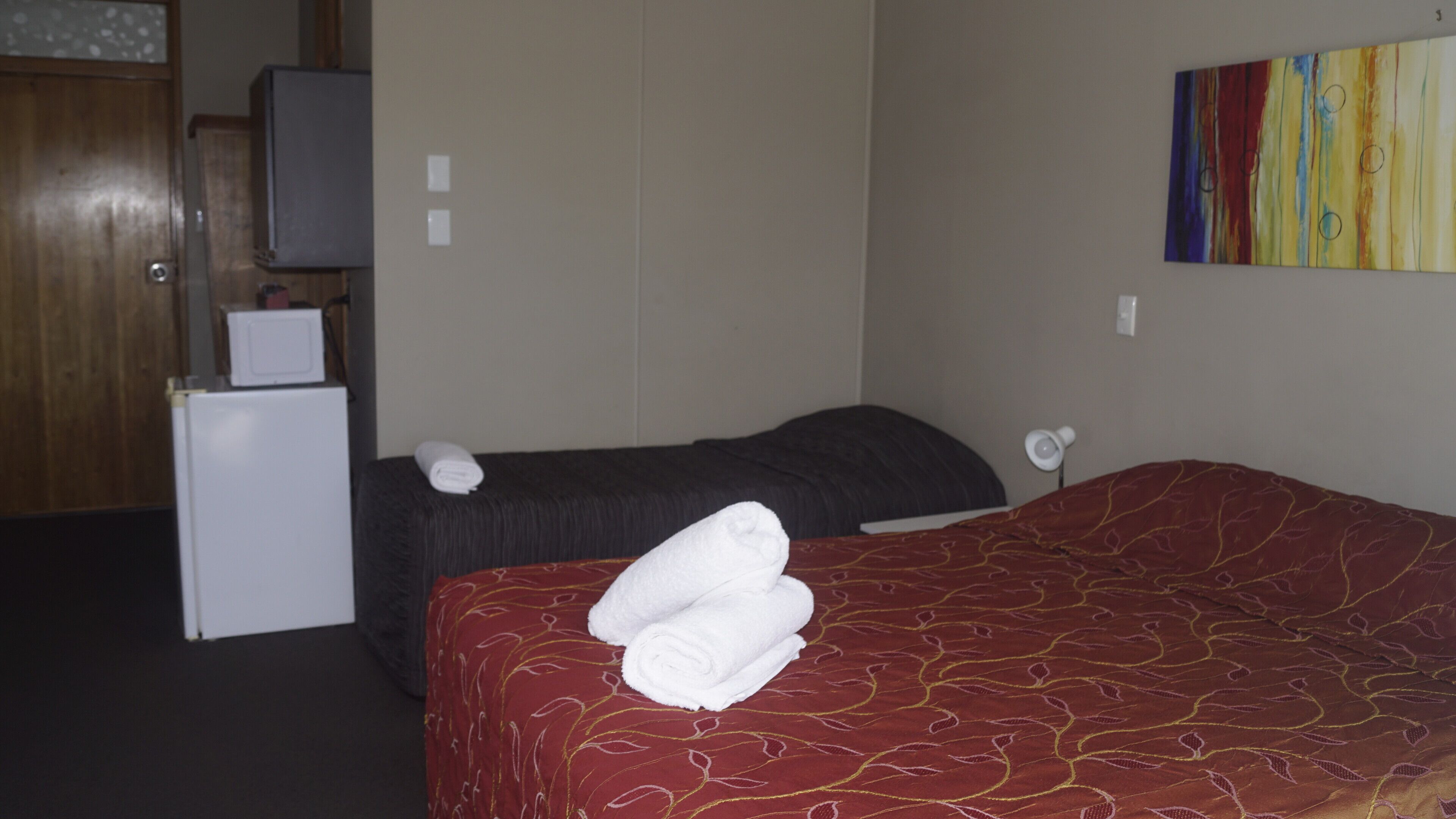 A hotel room with a bed, a small desk with a computer, a refrigerator, and a television.