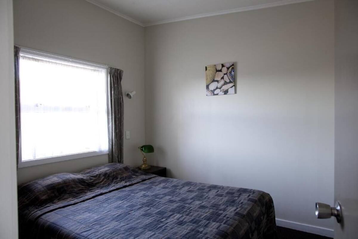 A bedroom with a bed, a window with curtains, a wall-mounted artwork, and a door.