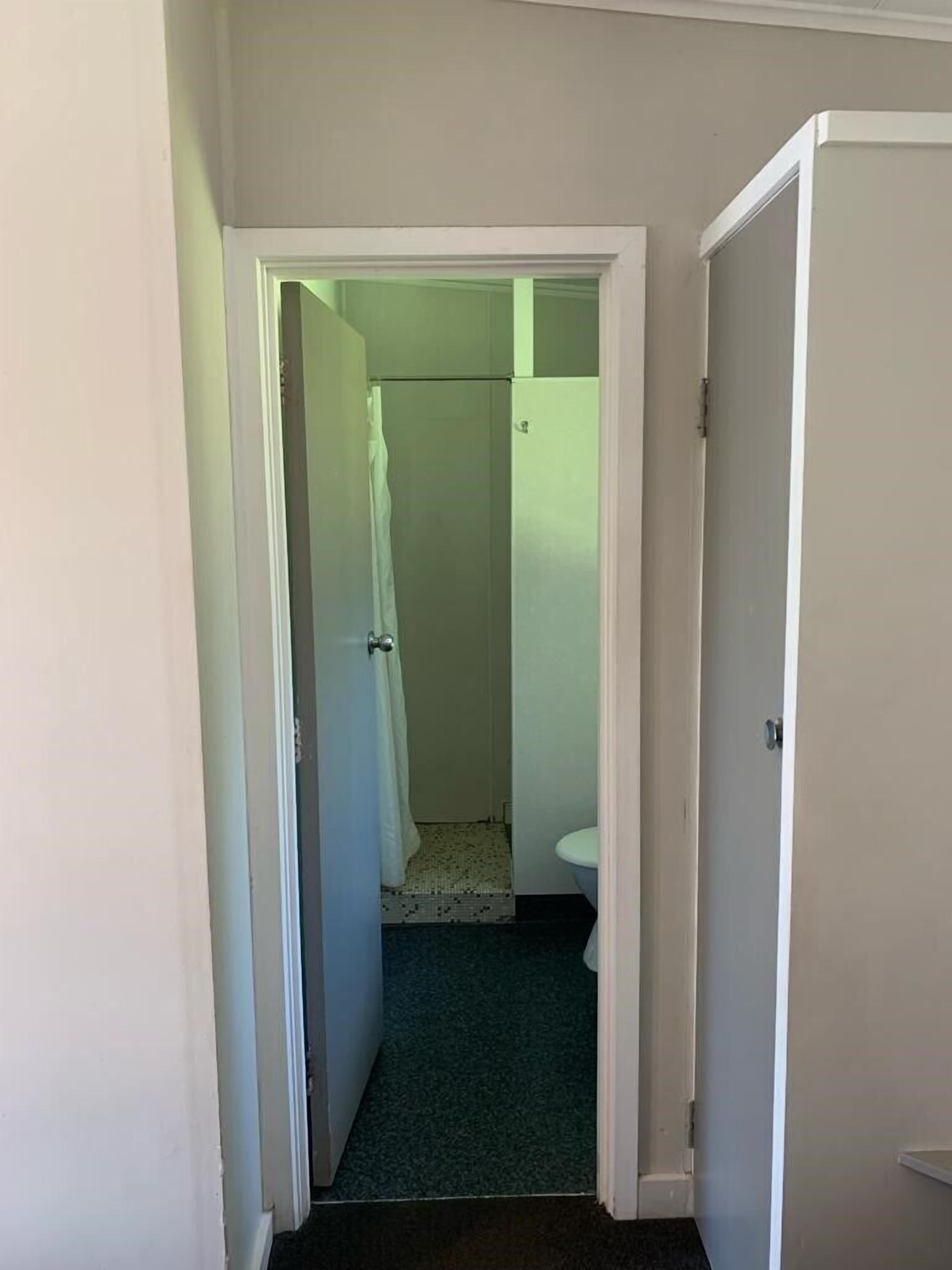 A narrow hallway leading to a bathroom with a toilet and a shower area.