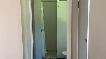 A narrow hallway leading to a bathroom with a toilet and a shower area.