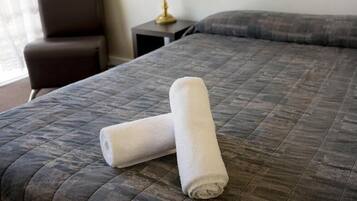 Una cama bien hecha con una colcha gris acolchada y dos toallas blancas enrolladas encima.