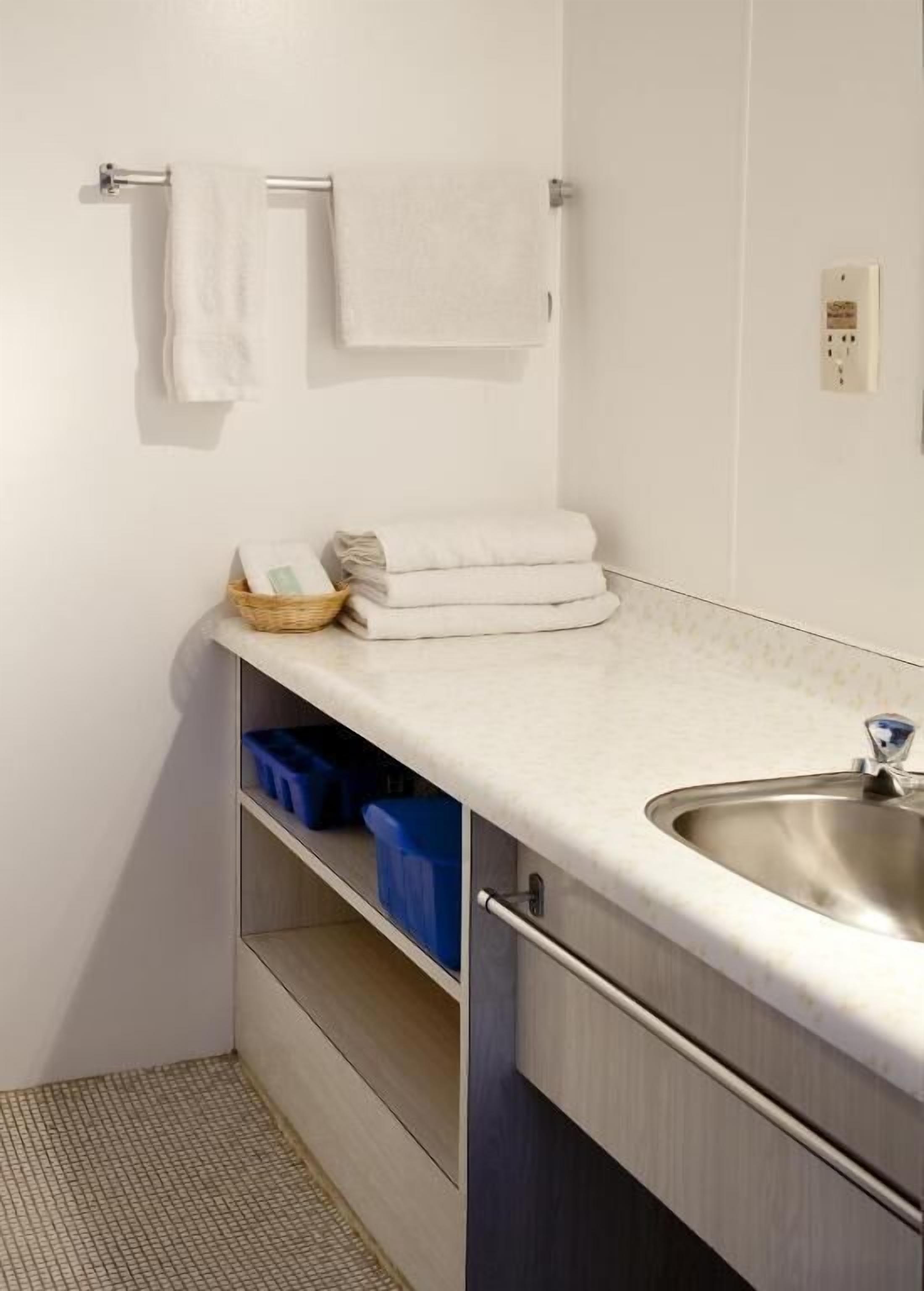 Un baño pequeño con un lavamanos, un perchero para toallas y un estante con toallas dobladas.