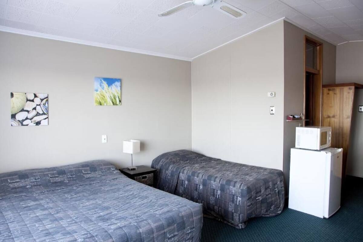 A room with two beds, a ceiling fan, a microwave, and a small table with a lamp.