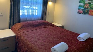A hotel room with a bed, a nightstand, a window with curtains, and a wall-mounted picture.
