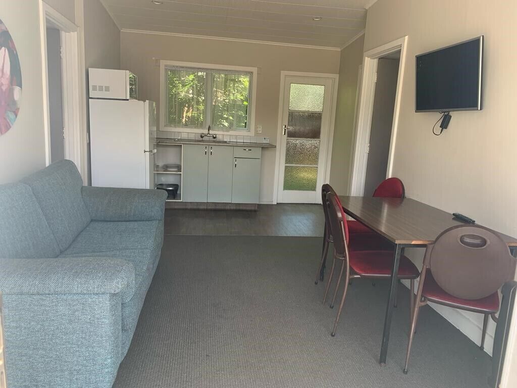 A compact living space with a kitchenette, a dining area with a table and chairs, and a television mounted on the wall.