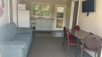 En kompakt opholdsstue med et tekøkken, et spiseområde med bord og stole, samt et fjernsyn ophængt på væggen.
