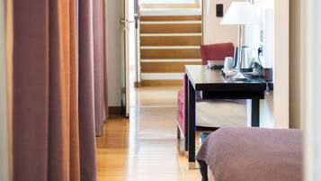 Una habitación de hotel con piso de madera, una cama, un escritorio con lámpara y vista a una escalera que lleva a otra habitación.