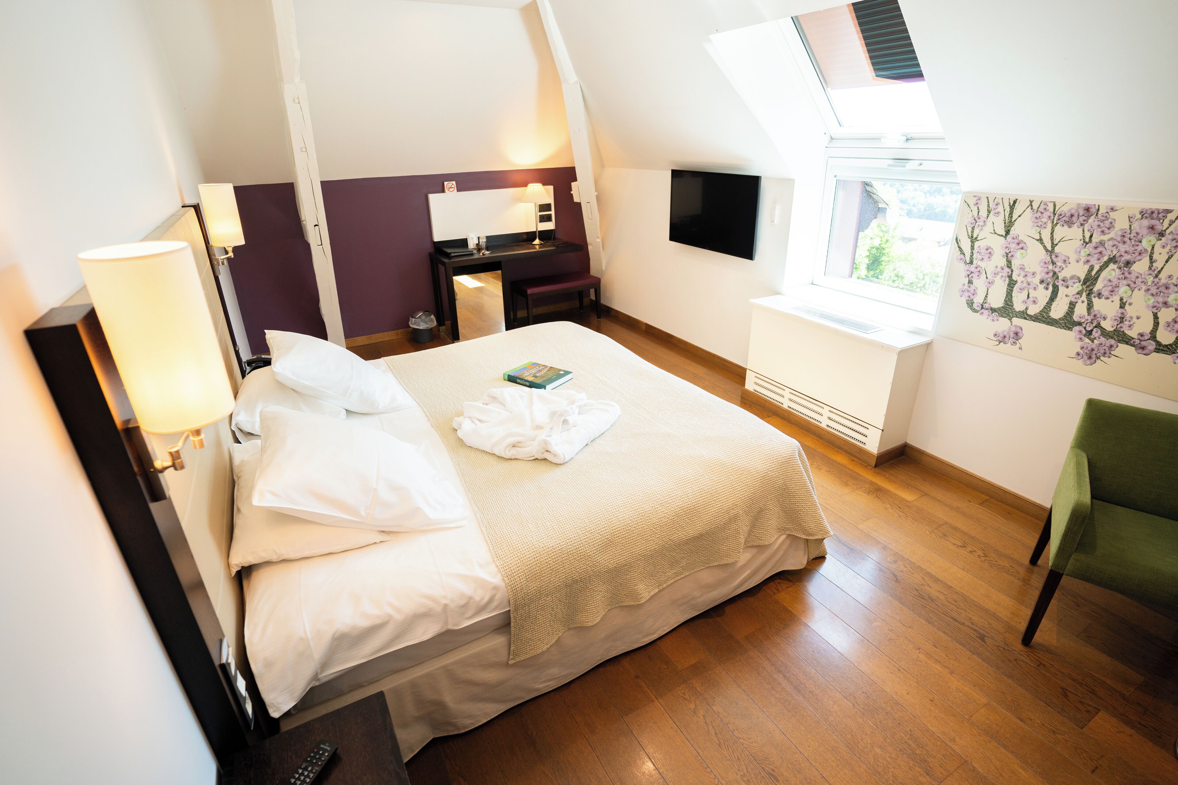 A hotel room with a bed, a desk, a chair, a TV, and a window.