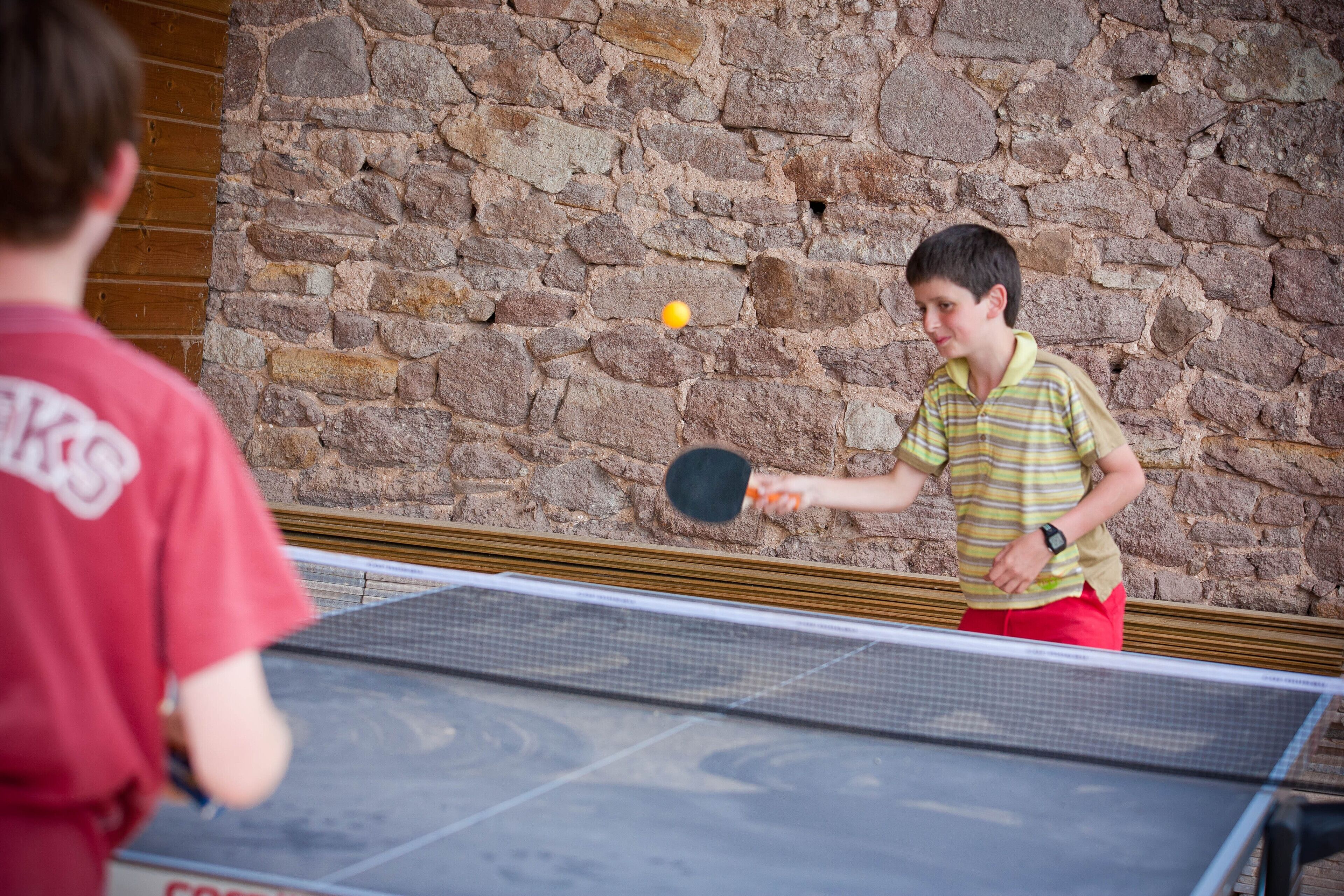 Un partido de ping pong en desarrollo frente a un fondo de pared de piedra.