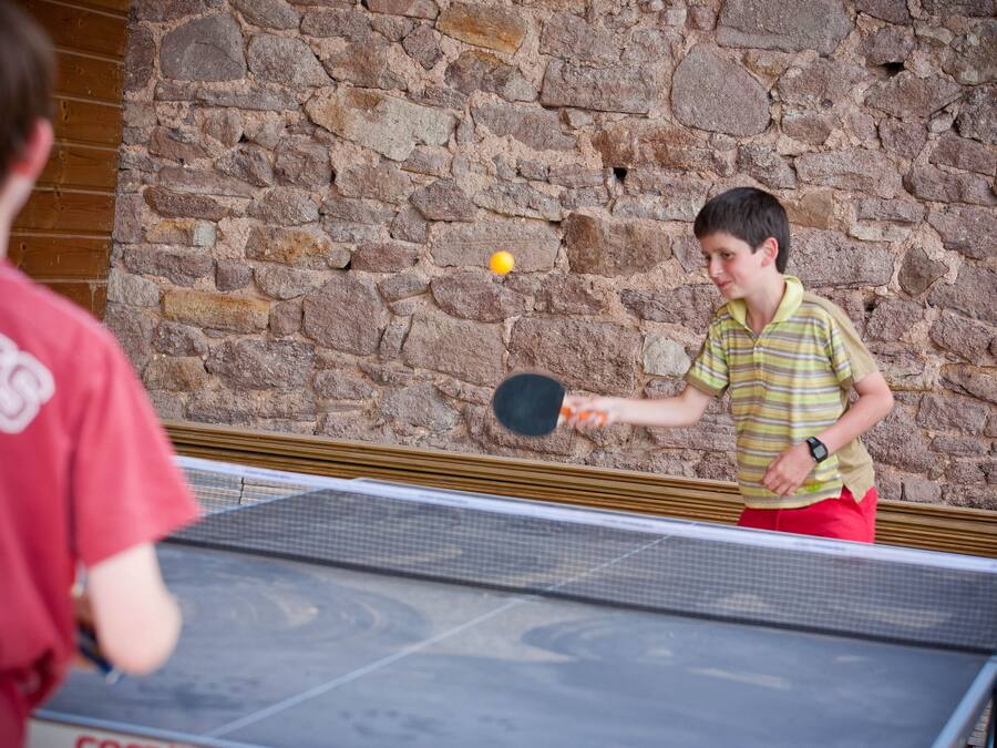A table tennis game in progress against a stone wall backdrop.