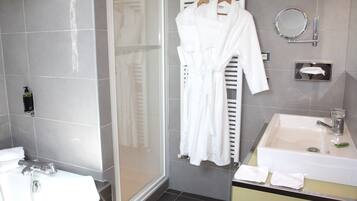 Een moderne badkamer met een douchecabine van glas, een wastafel met spiegel en een handdoekrek met badjassen.