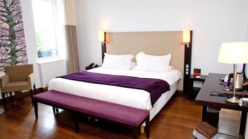 Een hotelkamer met een groot bed, een bankje, een bureau, een stoel en een nachtkastje.