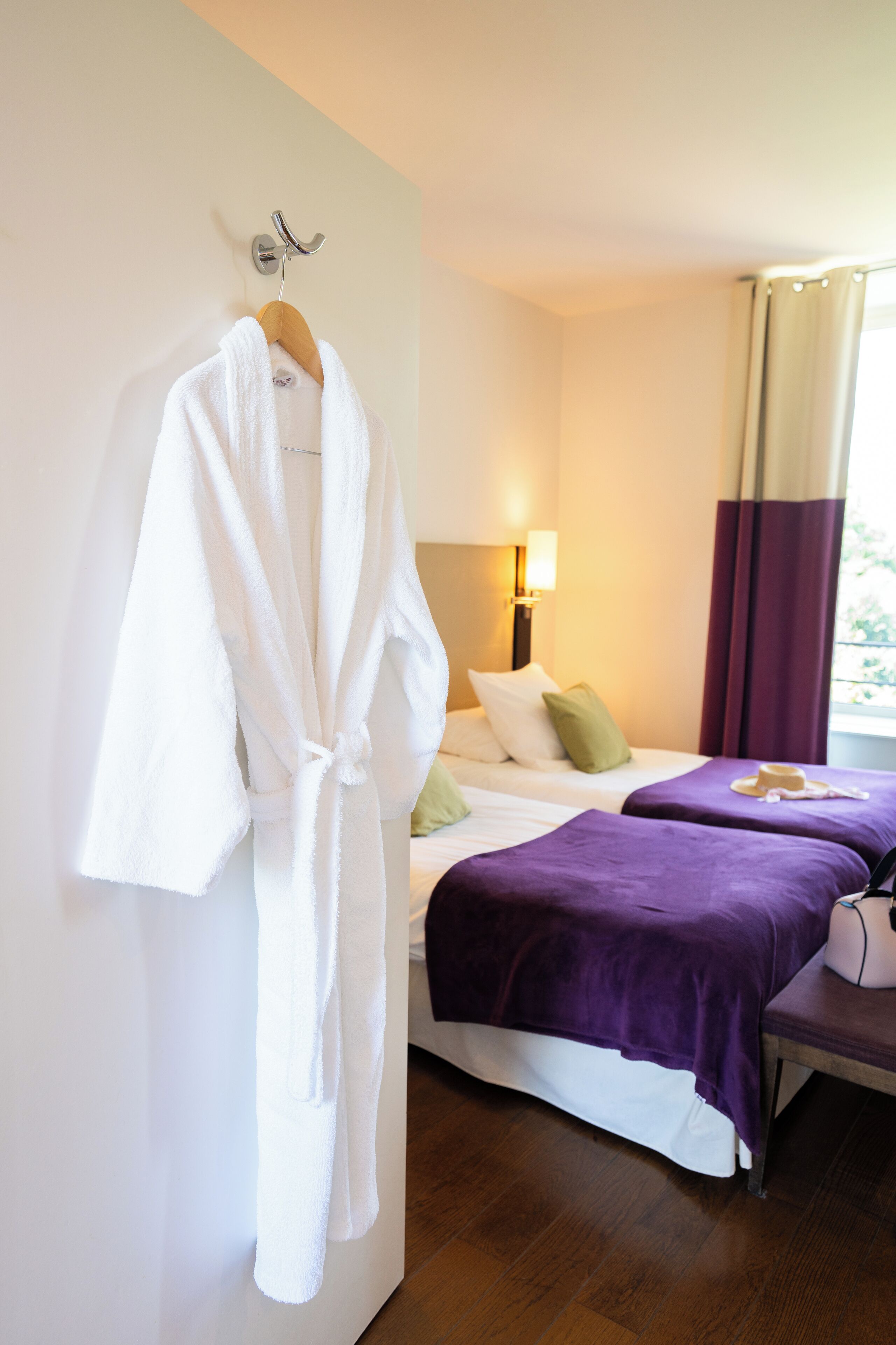 A hotel room with a bed, two bedside tables, a robe hanging on a hook, and a window with curtains.