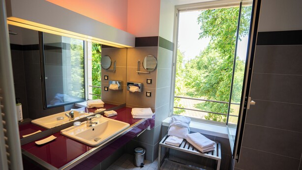 A modern bathroom with dual sinks, a large mirror, and a window with a view of greenery. - La Ferme de Bourran (Rodez)
