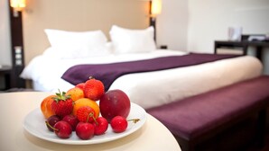 A hotel room with a neatly made bed, a bedside table with a fruit plate, and a nightstand with a lamp.