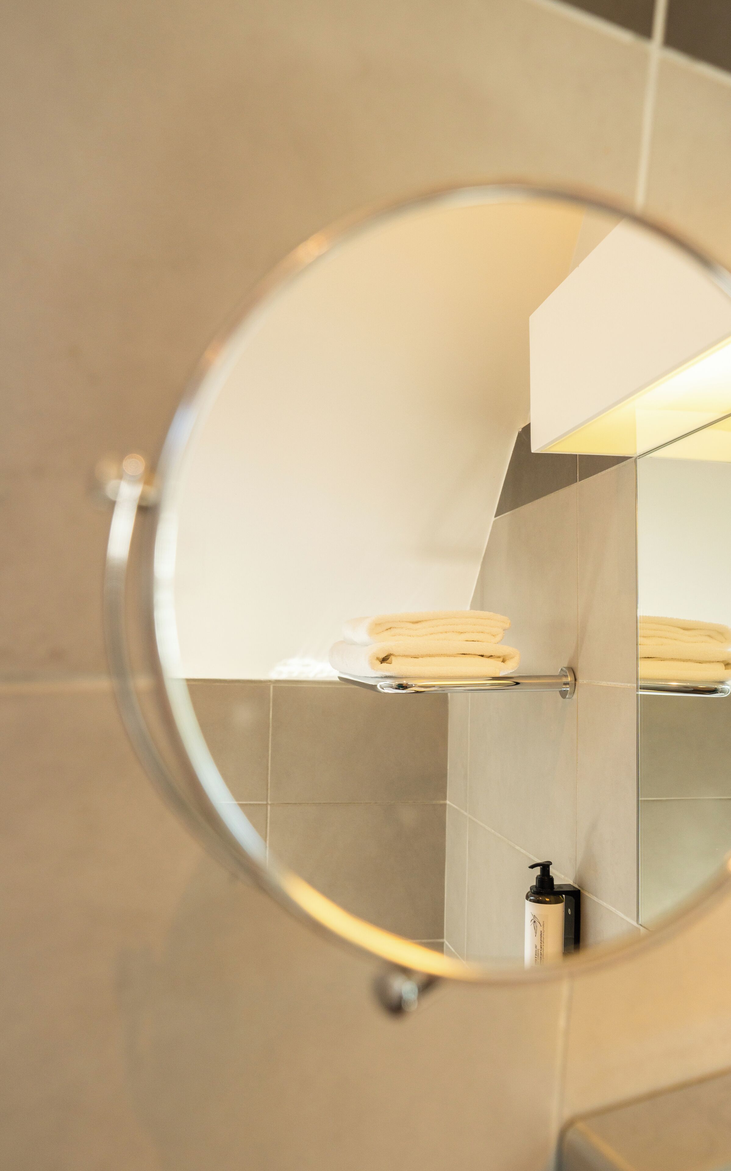 Une salle de bain avec un miroir rond, un porte-serviettes avec des serviettes pliées et une bouteille de shampoing.