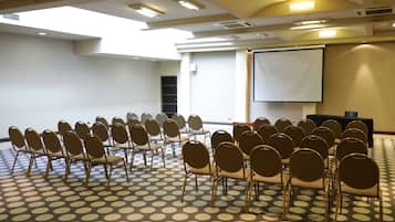 Un salón de conferencias con suelo estampado, filas de sillas, una pantalla de proyector y un atril.