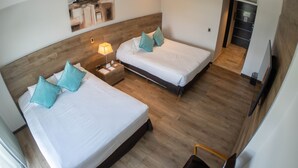 A hotel room with two beds, wooden flooring, a nightstand with a lamp, and a painting on the wall. - Mod Hotels Mendoza (Mendoza)