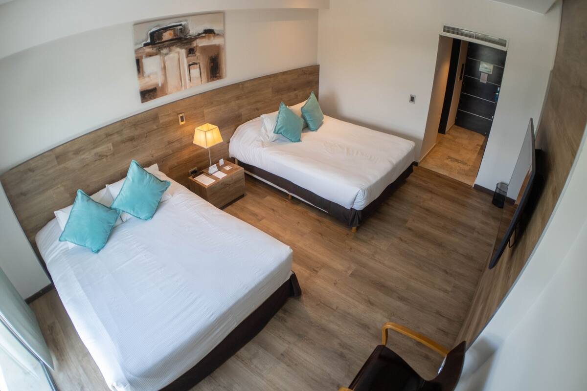 Ein Hotelzimmer mit zwei Betten, Holzboden, einem Nachttisch mit Lampe und einem Bild an der Wand.