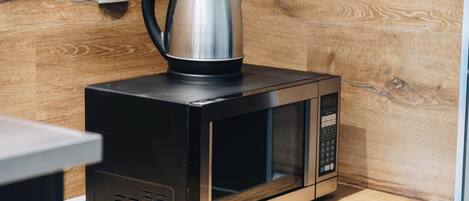 Un horno microondas con una tetera encima, sobre una encimera de madera.