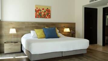 A modern hotel room with a large bed, two bedside lamps, a wooden headboard, and a colorful abstract painting on the wall.