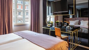 Habitación de hotel con cama, escritorio, silla, televisor y vistas a edificios.