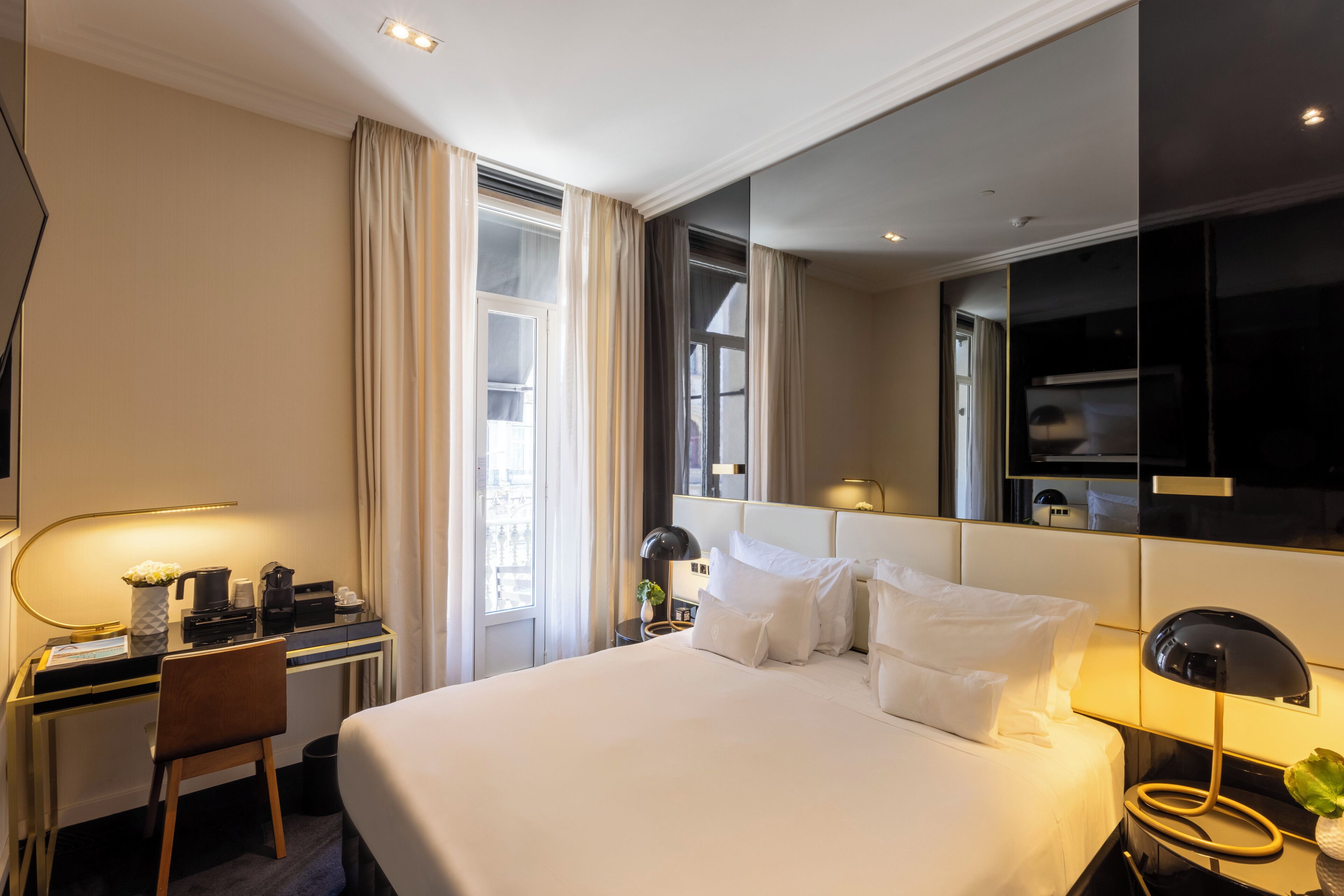 A hotel room with a bed, desk, chair, and a large mirror.