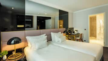A modern hotel room with a large bed, bedside table, lamp, and a desk with a chair.