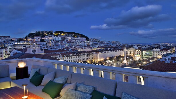 Una terraza en la azotea con vistas a la ciudad, una mesa con una vela y un sofá con cojines estampados.