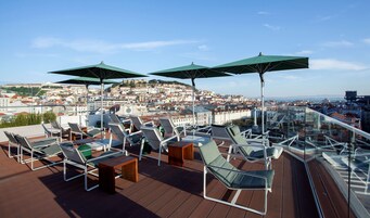 En tagterrasse med liggestole, parasoller og udsigt over byen.