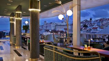 Um restaurante moderno com pé-direito alto, janelas amplas e vista para uma cidade histórica.