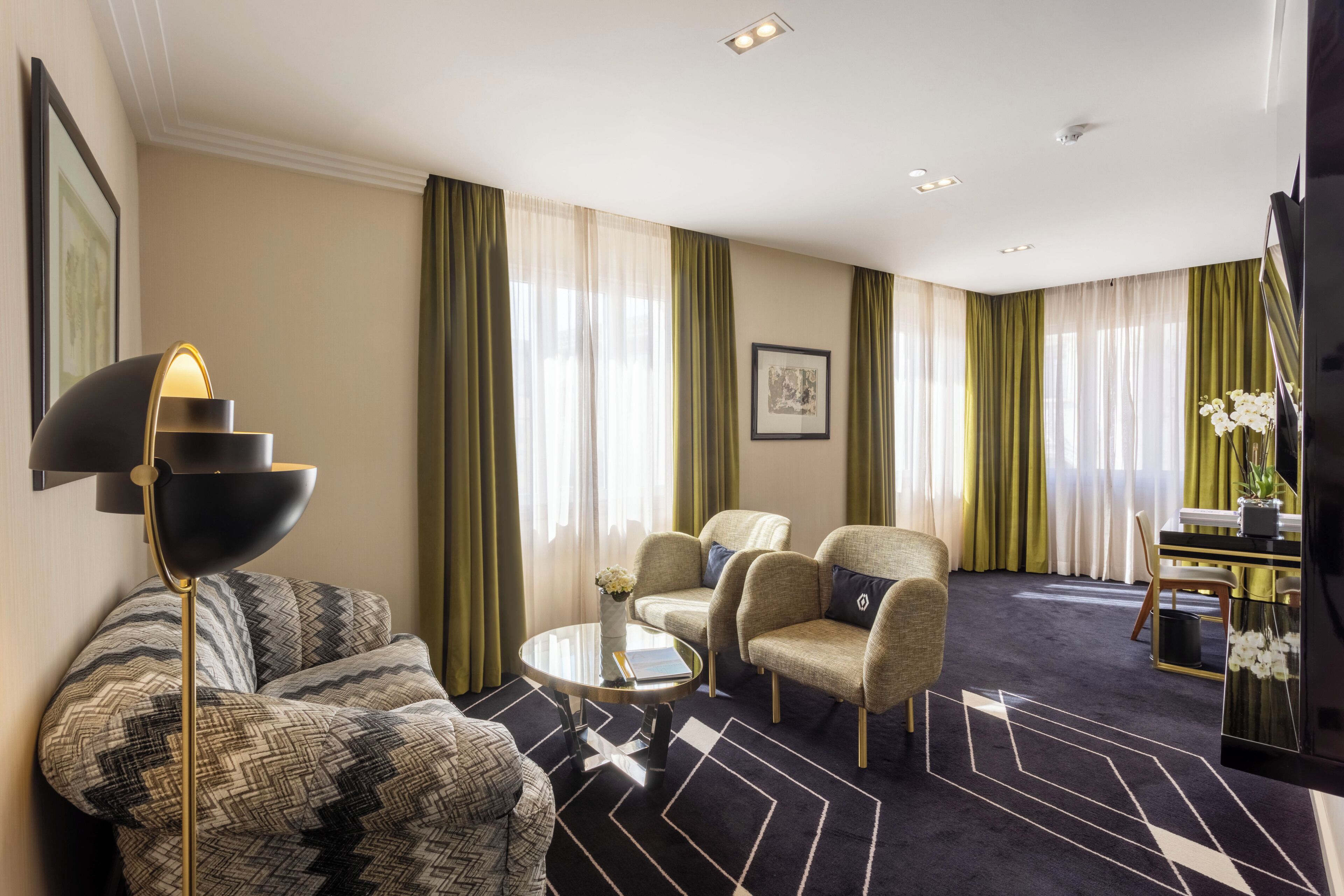 Une chambre d’hôtel équipée d’un canapé, de fauteuils, d’une petite table, d’un lampadaire et d’un téléviseur.