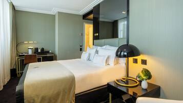 A hotel room with a large bed, a desk, a chair, a lamp, and a mirror.