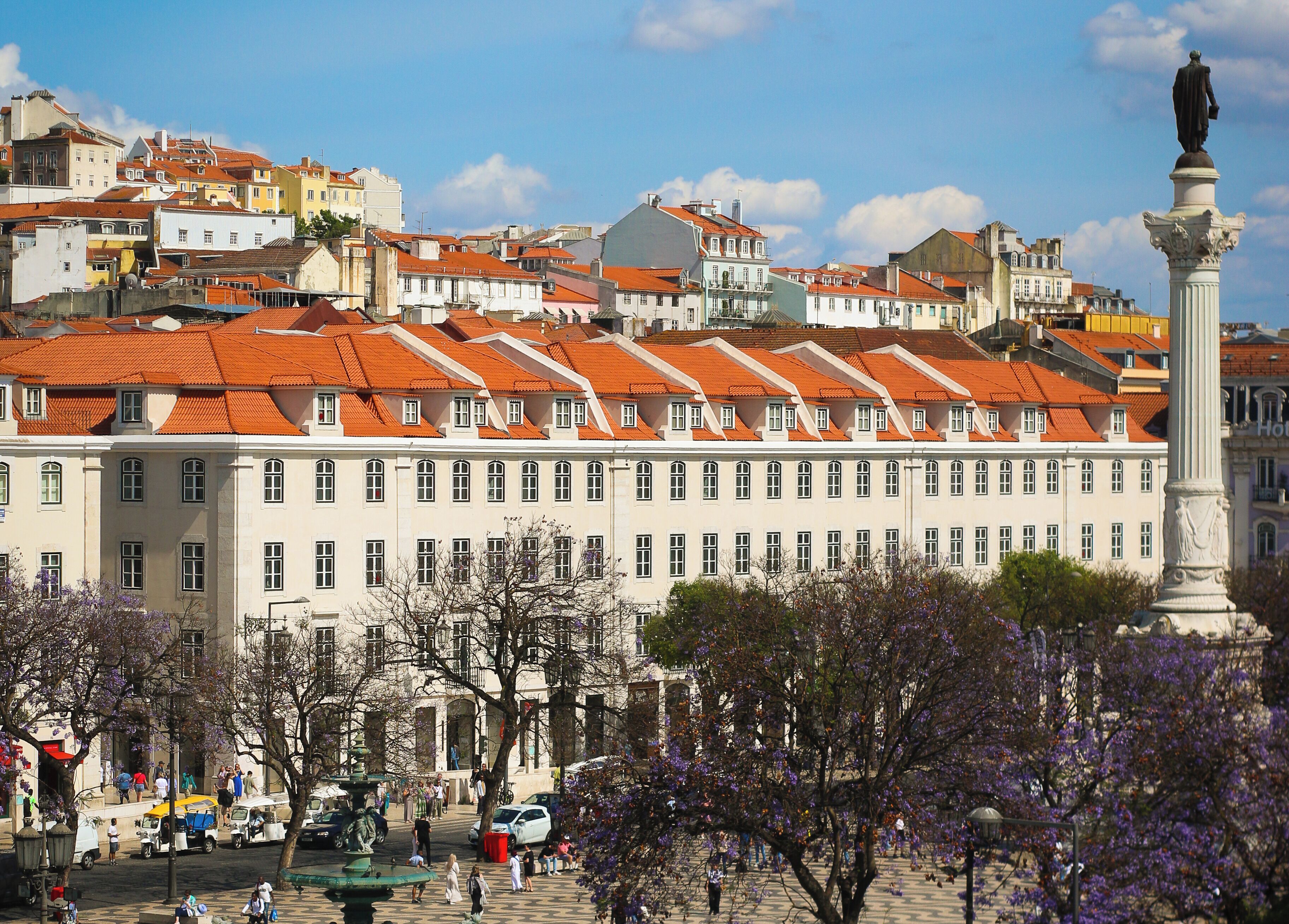 A historic building with a row of red-tiled roofs and a statue in the foreground.