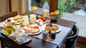 Une table de petit-déjeuner avec divers aliments, un verre de jus d’orange, une bouteille de lait et une vue sur la verdure à l’extérieur.