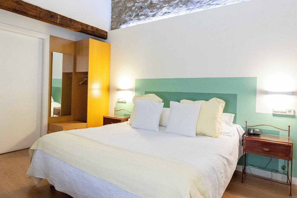 Un dormitorio con una cama grande, un armario de madera, un espejo, una mesita de noche y un tragaluz.