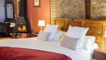 Habitación de hotel con una cama grande, cabecera de madera, pared de piedra, chimenea y mesita de noche con lámpara.