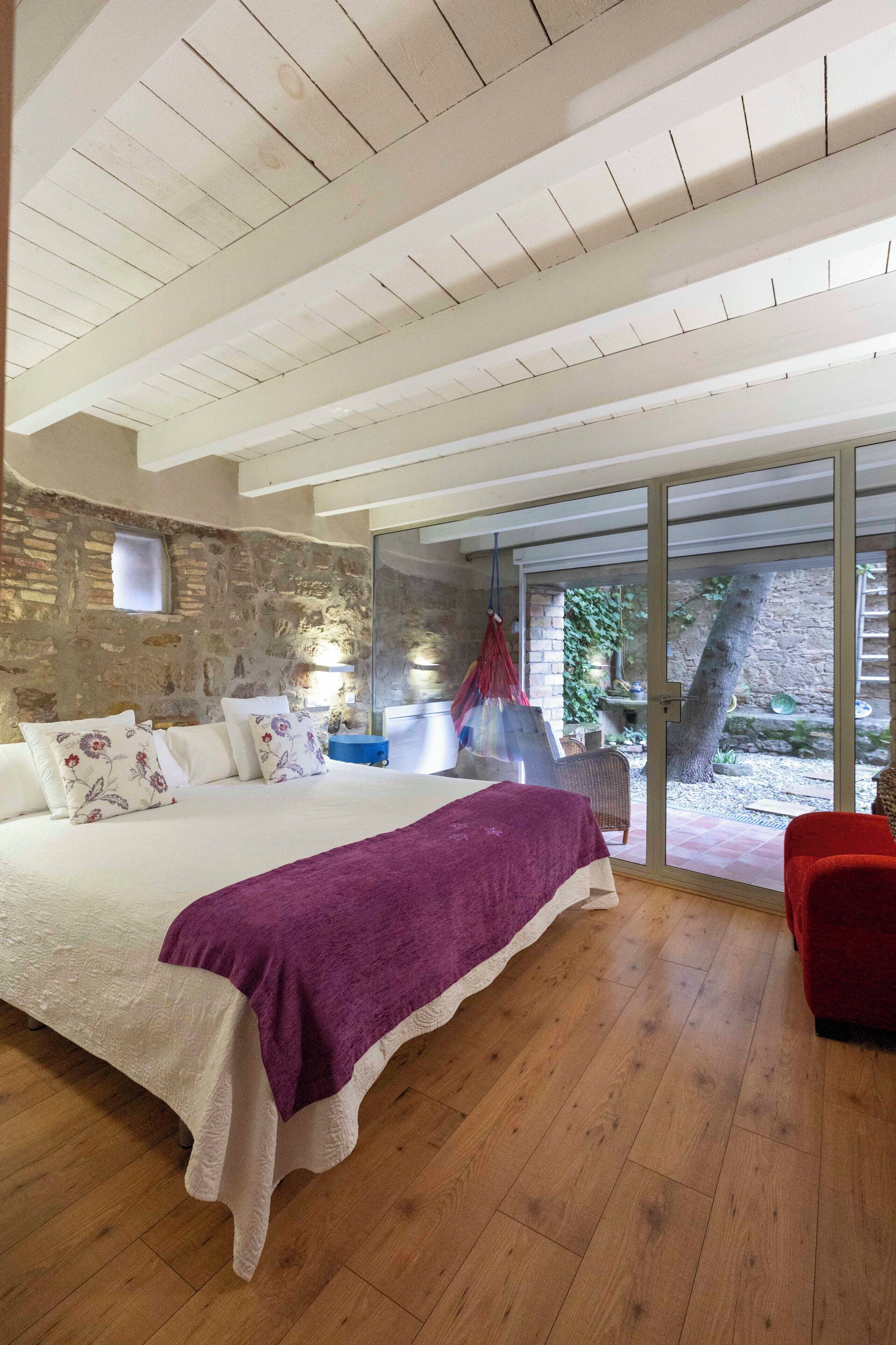 A bedroom with a large bed, a hanging chair, and a view of the outdoors through a glass door.