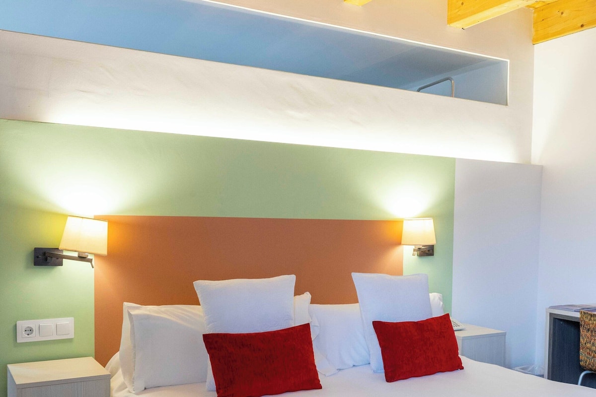 Una habitación de hotel moderna con una cama grande, dos mesitas de noche y techo de madera.