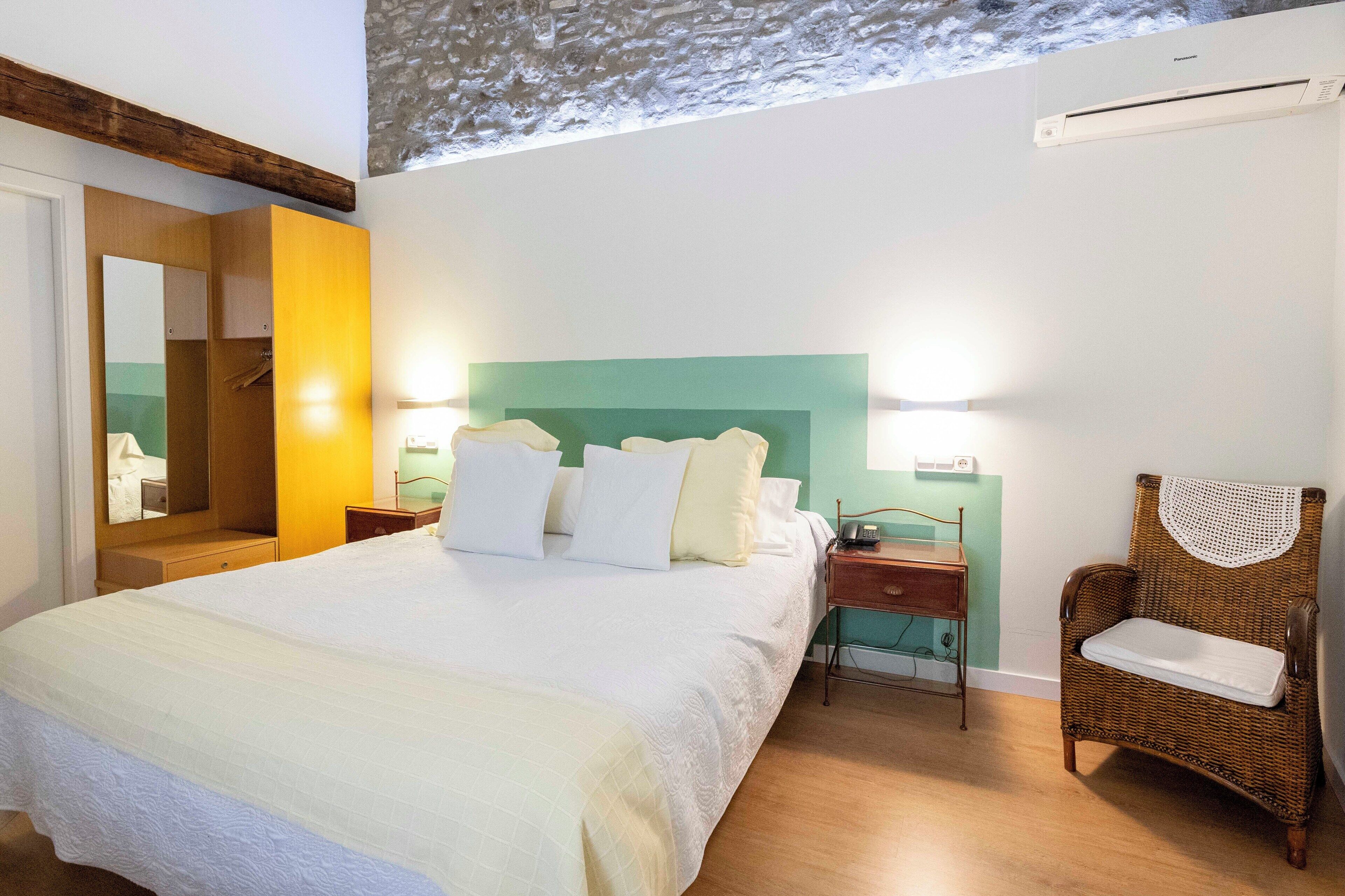 Un dormitorio con una cama grande, mesitas de noche, una silla de mimbre y un espejo.