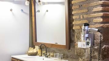 A bathroom with a stone wall, a wooden vanity with a mirror, a hairdryer, and a stack of towels.