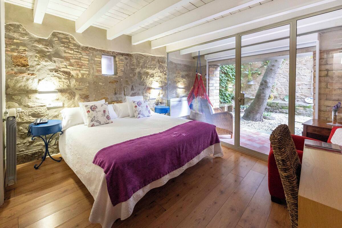 Un dormitorio con una cama grande, una pared de piedra, suelo de madera y vistas al exterior a través de un ventanal.