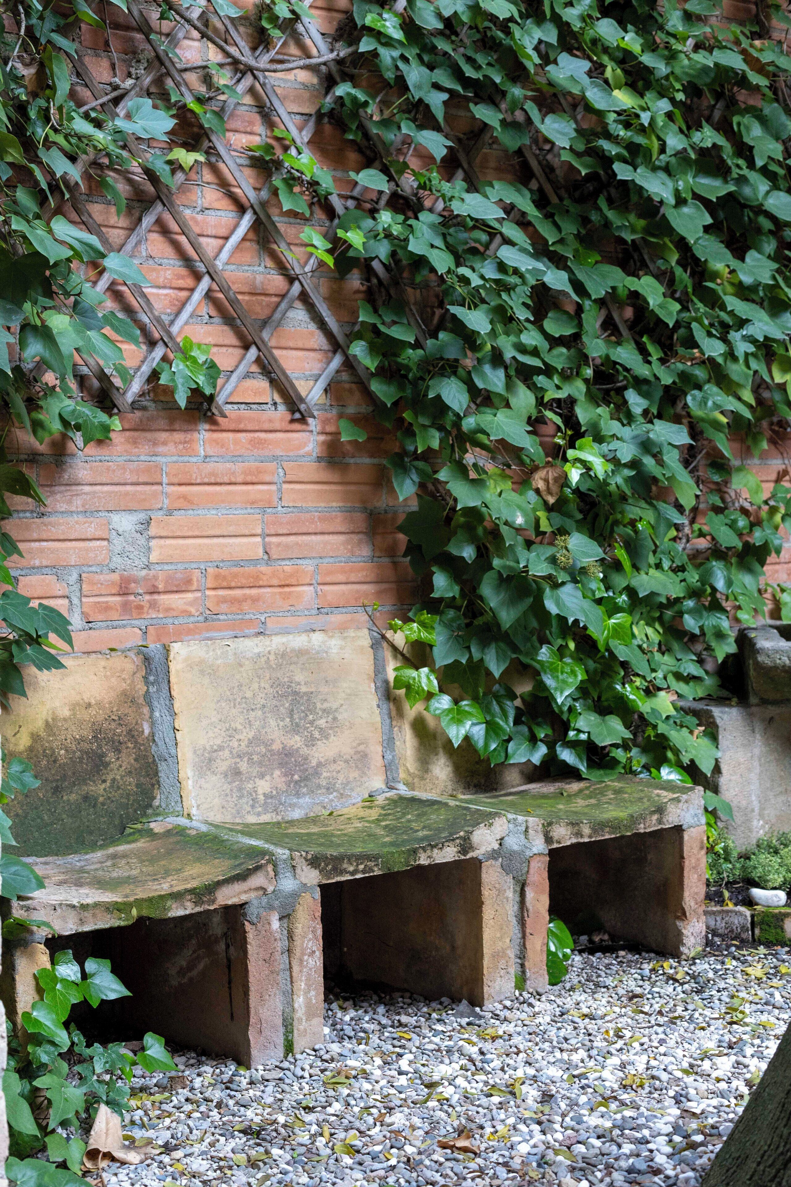 Paredes de tijolo com treliça, um banco de pedra e um caminho de cascalho.