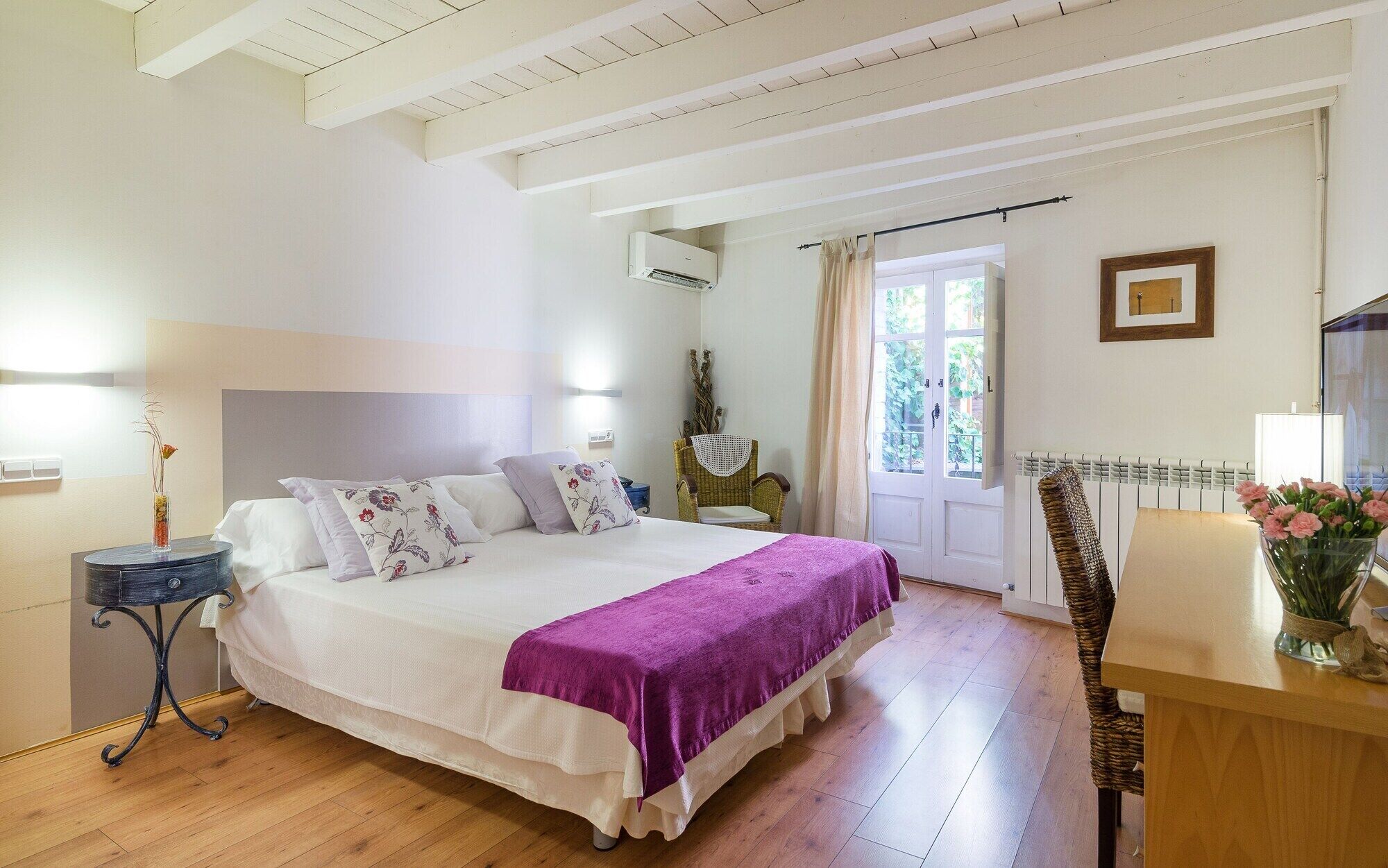 Un dormitorio con cama, mesita de noche, silla y ventana con cortinas.