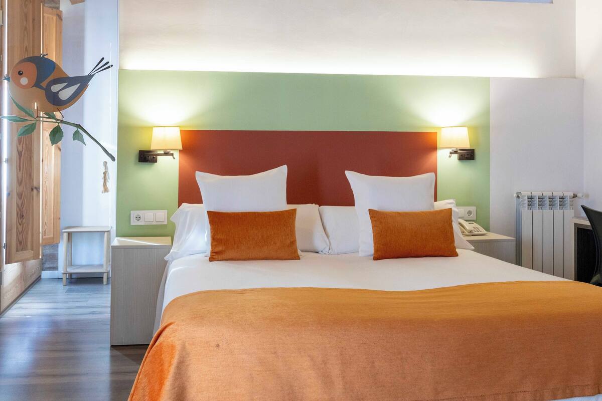 Una habitación de hotel con una cama grande, dos lámparas de noche, un teléfono y un radiador.