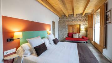 Een hotelkamer met een groot bed, een stenen muur, houten balken, een rode bank en een stenen open haard.