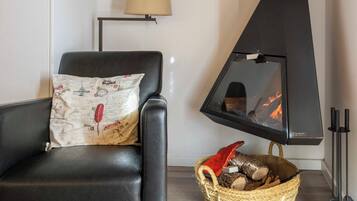A cozy room with a black leather chair, a woven basket of firewood, and a black wood stove with visible flames.