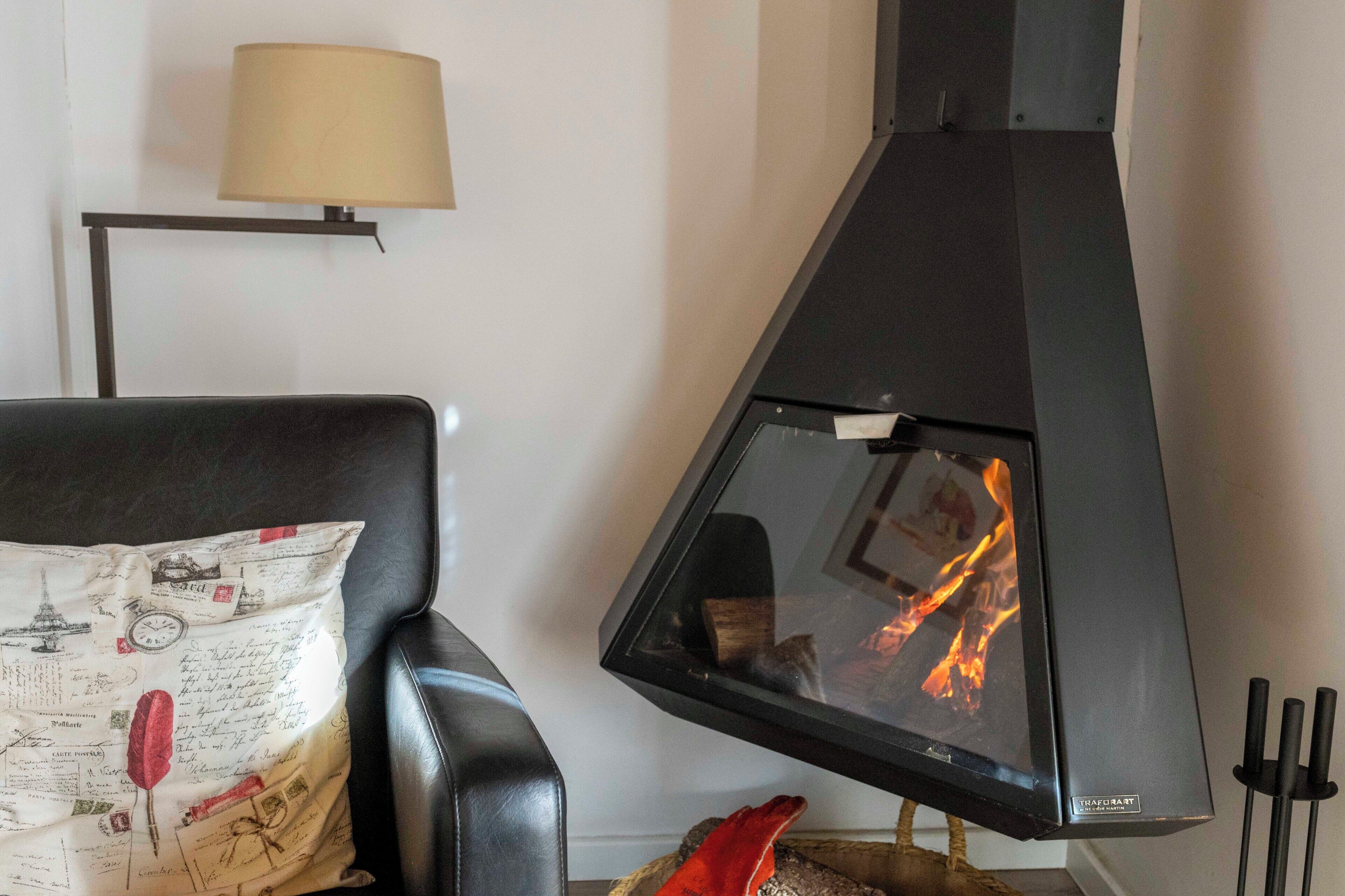 Una sala de estar moderna con un sofá de cuero negro, un cojín decorativo, un hogar a leña con puerta de vidrio y una lámpara de pie.